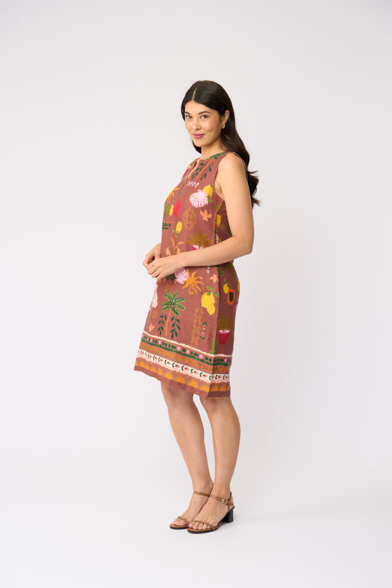 Foil clothing modeling a sleeveless brown dress with a colorful tropical and floral print, standing against a plain white studio background.