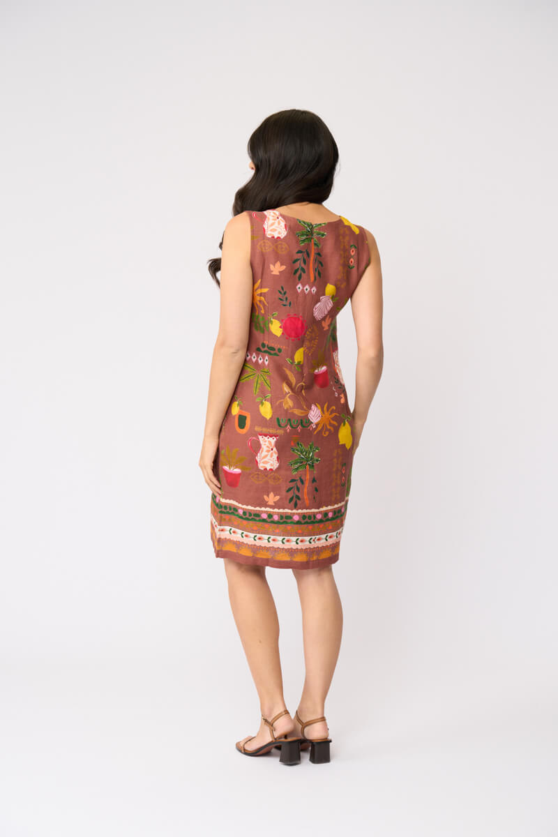 Foil clothing modeling a sleeveless brown dress with a colorful tropical and floral print, standing against a plain white studio background. Back view.