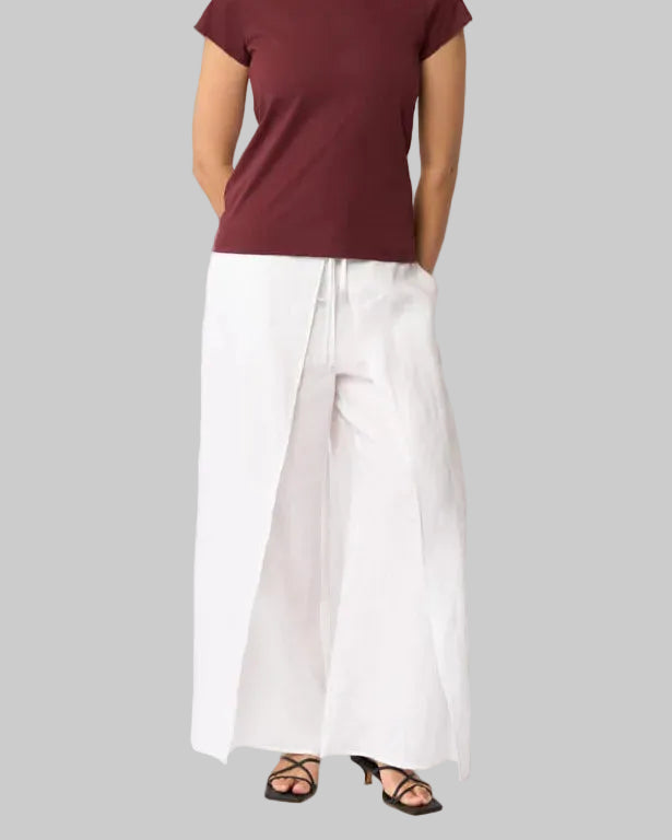 Foil clothing  model in a short-sleeve crewneck t-shirt in burgundy, paired with white wide-leg pants with overlay and black sandals, standing against a plain white studio background.