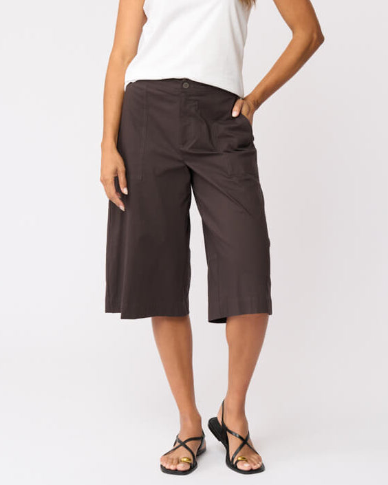 Foil clothing modeling a white short-sleeve t-shirt and dark brown wide-leg cropped pants with black strappy sandals, standing against a light gray studio background.