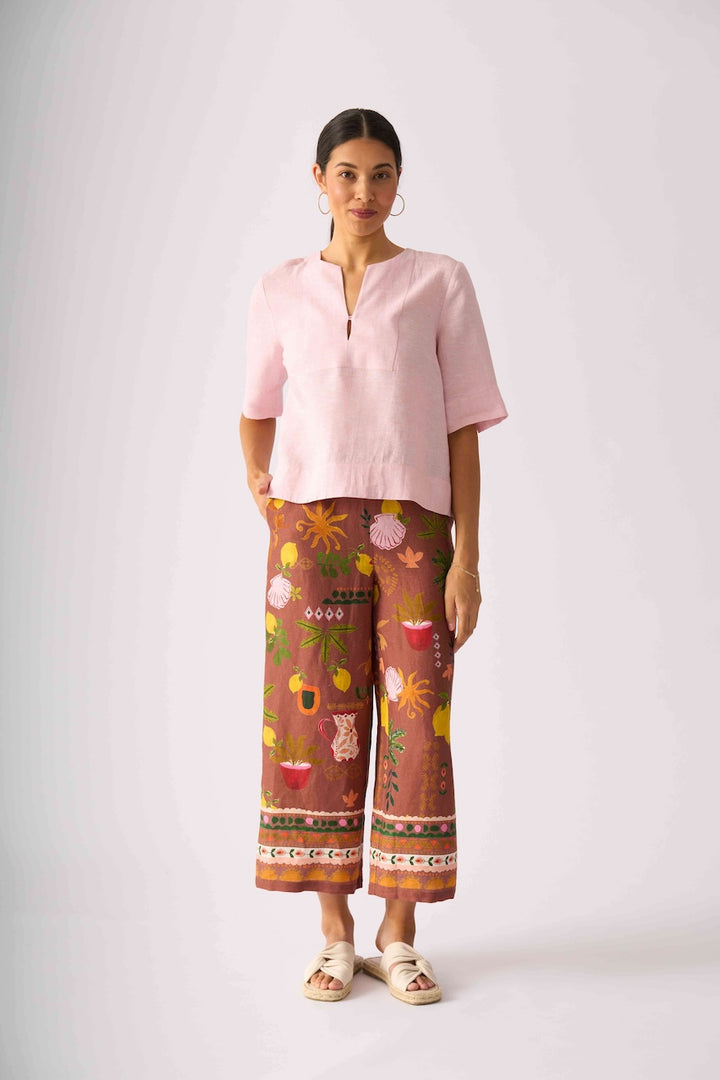 Foil clothing,  modeling a light pink short-sleeve top and brown wide-leg pants with a colorful floral and botanical print, standing against a light gray studio background.