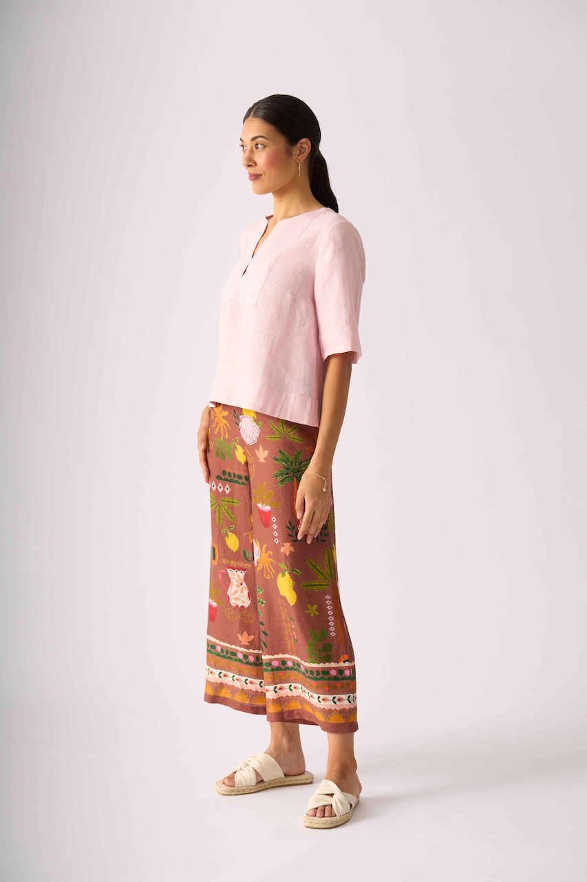 Foil clothing,  modeling a light pink short-sleeve top and brown wide-leg pants with a colorful floral and botanical print, standing against a light gray studio background.