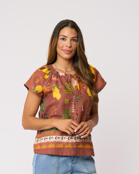 Foil Clothing, modeling a short-sleeve top with a brown, orange, and yellow patterned print, paired with light blue wide-leg jeans and brown sandals, against a plain light gray background.