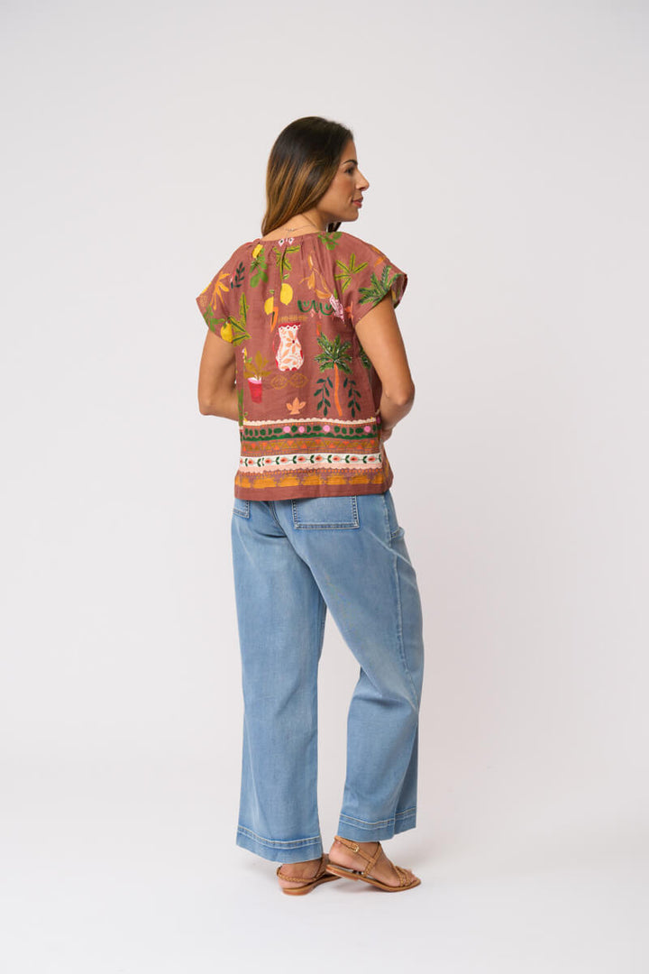 Foil Clothing, modeling a short-sleeve top with a brown, orange, and yellow patterned print, paired with light blue wide-leg jeans and brown sandals, against a plain light gray background.