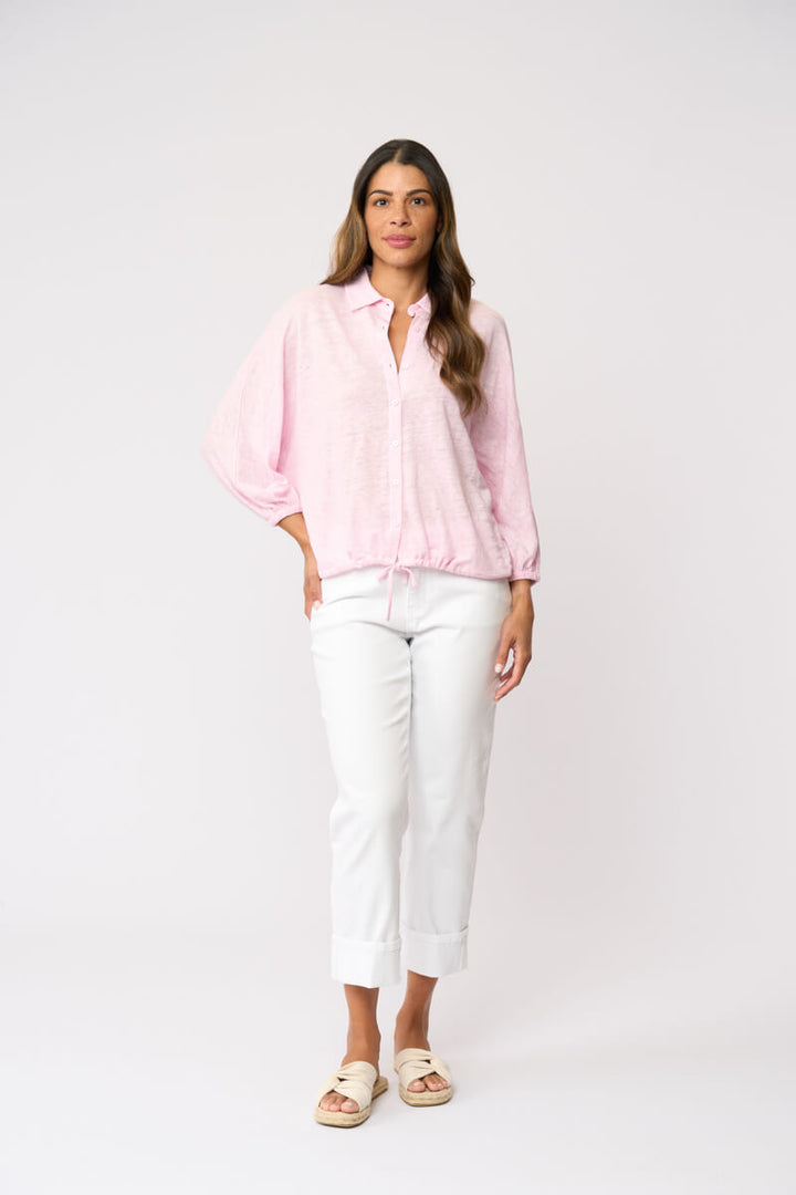 Foil clothing modeling a light pink long-sleeve button-up shirt with white cropped pants and beige slide sandals, standing against a plain white studio background.