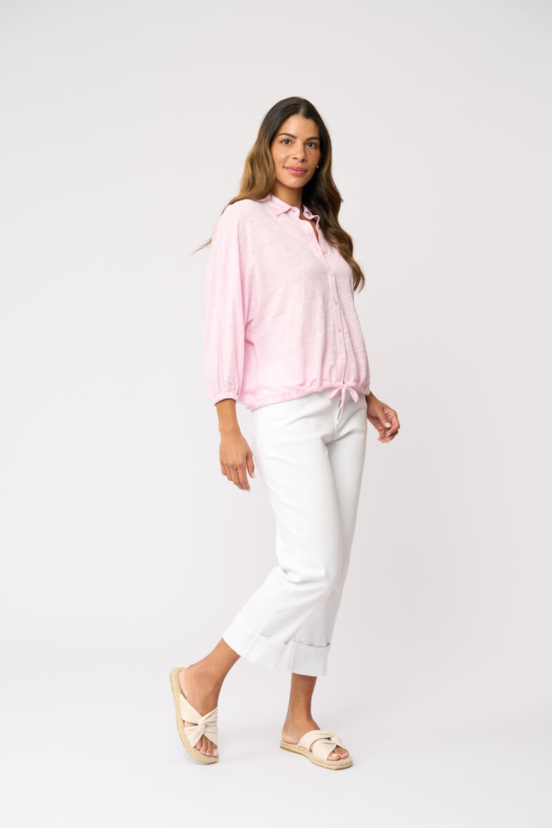 Foil clothing modeling a light pink long-sleeve button-up shirt with white cropped pants and beige slide sandals, standing against a plain white studio background.