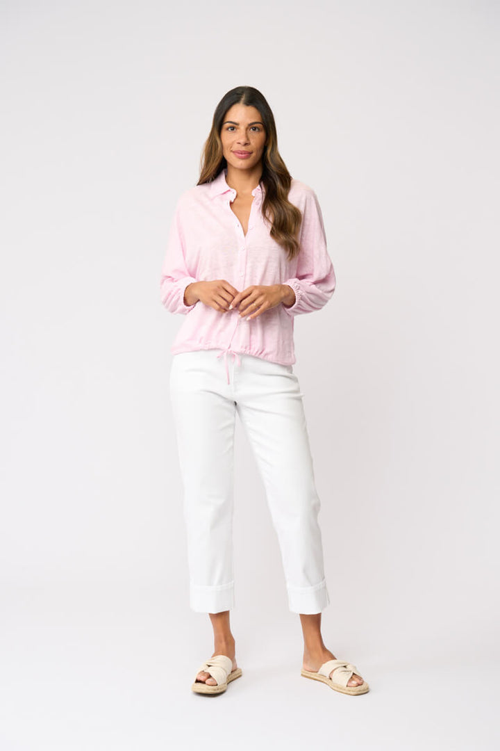 Foil clothing modeling a light pink long-sleeve button-up shirt with white cropped pants and beige slide sandals, standing against a plain white studio background.