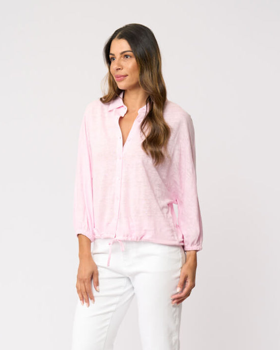 Foil clothing modeling a light pink long-sleeve button-up shirt with white cropped pants, standing against a plain white studio background.