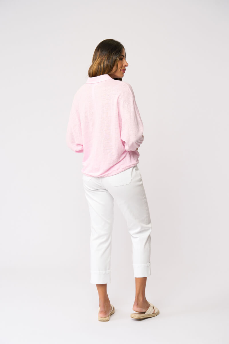 Foil clothing modeling a light pink long-sleeve button-up shirt with white cropped pants and beige slide sandals, standing against a plain white studio background. Back view.