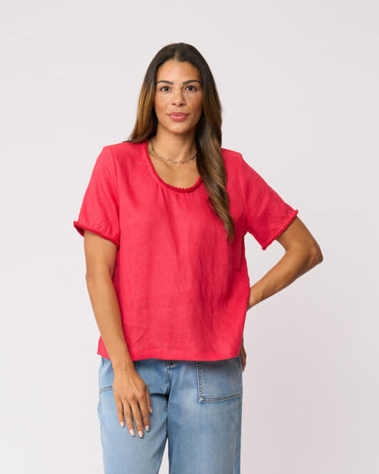 Foil clothing model in a bright coral pink short-sleeve linen top and wide-leg light blue jeans against a plain white studio background.