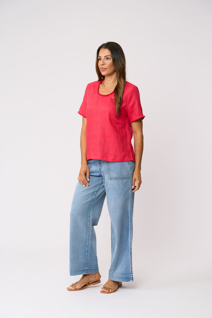 Foil clothing model in a bright coral pink short-sleeve linen top and wide-leg light blue jeans against a plain white studio background.