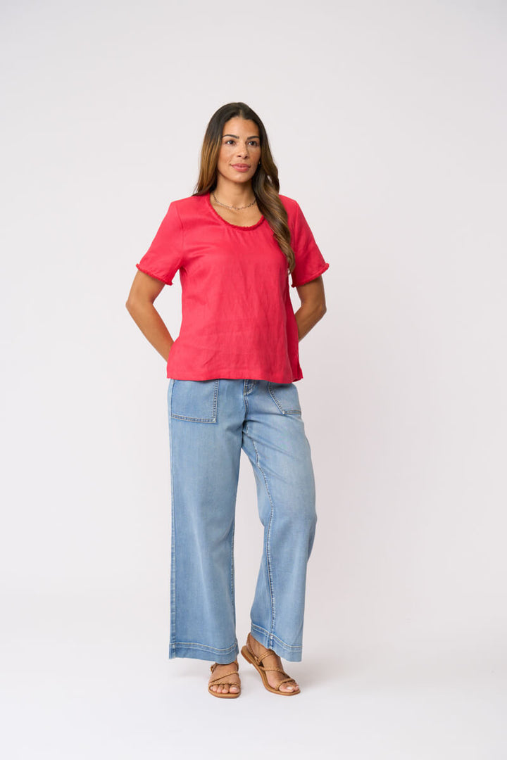 Foil clothing model in a bright coral pink short-sleeve linen top and wide-leg light blue jeans against a plain white studio background.