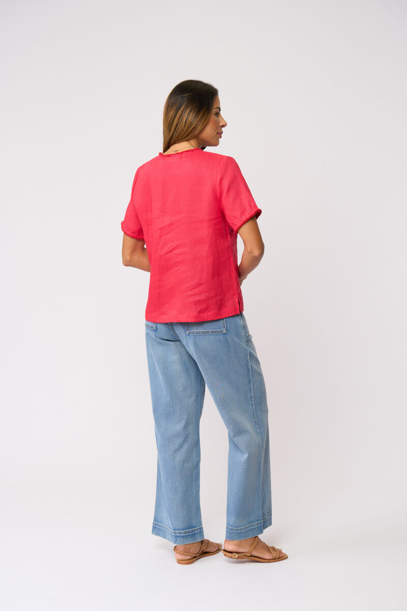 Foil clothing model in a bright coral pink short-sleeve linen top and wide-leg light blue jeans against a plain white studio background. Back view