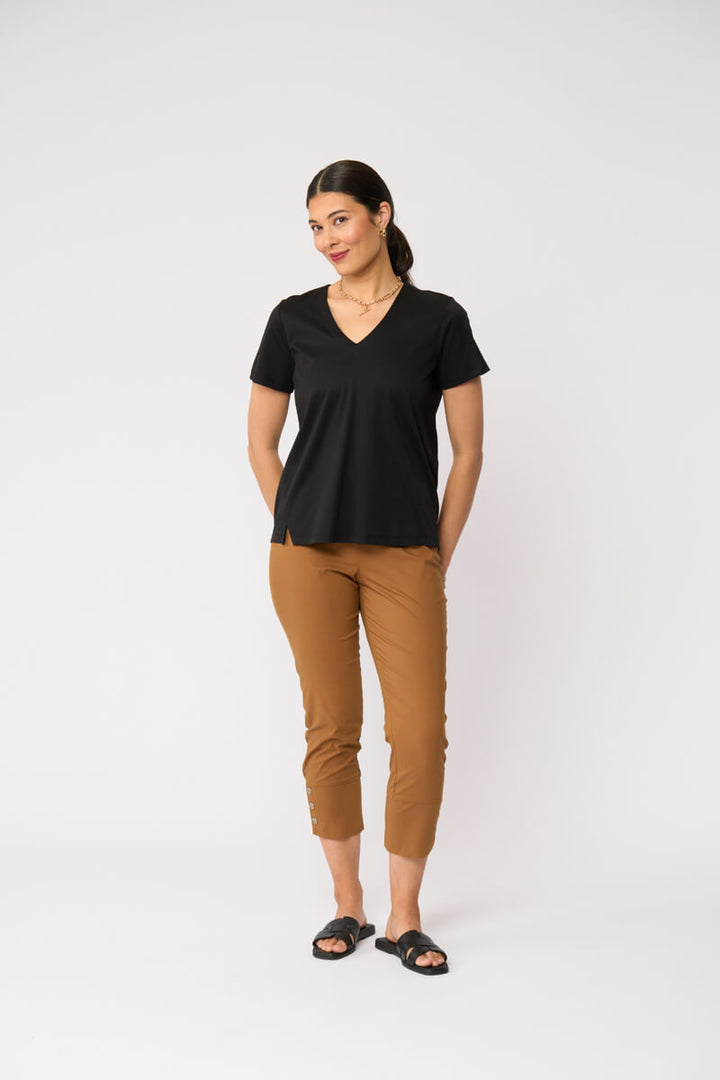Foil model in a black short-sleeve V-neck t-shirt and cropped tan umber pants with black slide sandals, standing against a plain light gray studio background.