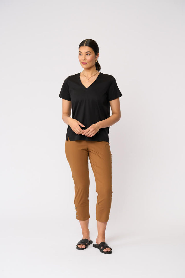 Foil model in a black short-sleeve V-neck t-shirt and cropped tan umber pants with black slide sandals, standing against a plain light gray studio background.