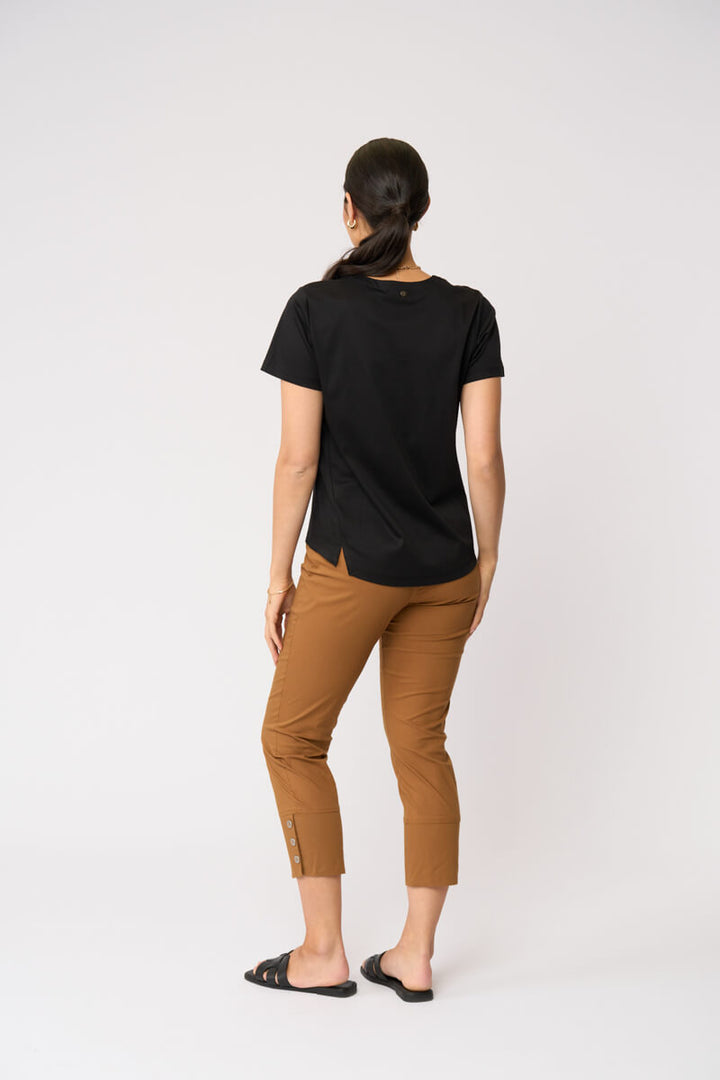 Foil model in a black short-sleeve V-neck t-shirt and cropped tan umber pants with black slide sandals, standing against a plain light gray studio background. Back view