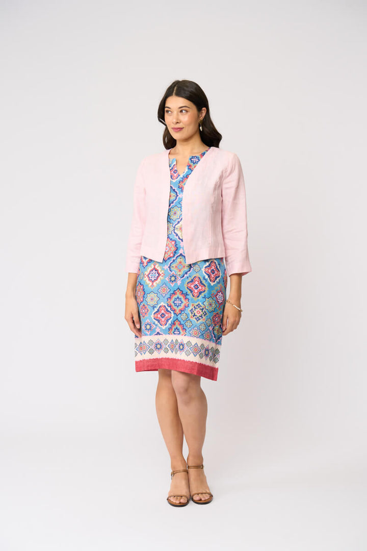 Foil model in a light pink cardigan over a blue and red patterned dress, standing against a plain white studio background.