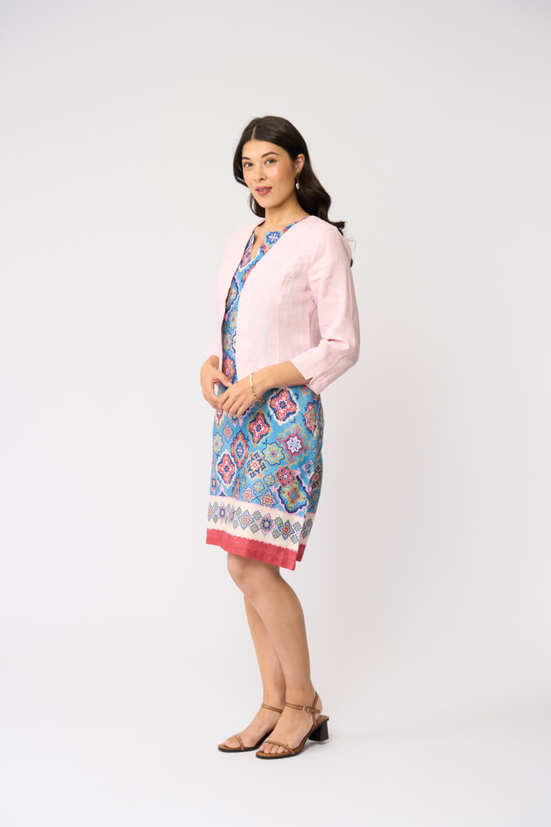 Foil model in a light pink cardigan over a blue and red patterned dress, standing against a plain white studio background.