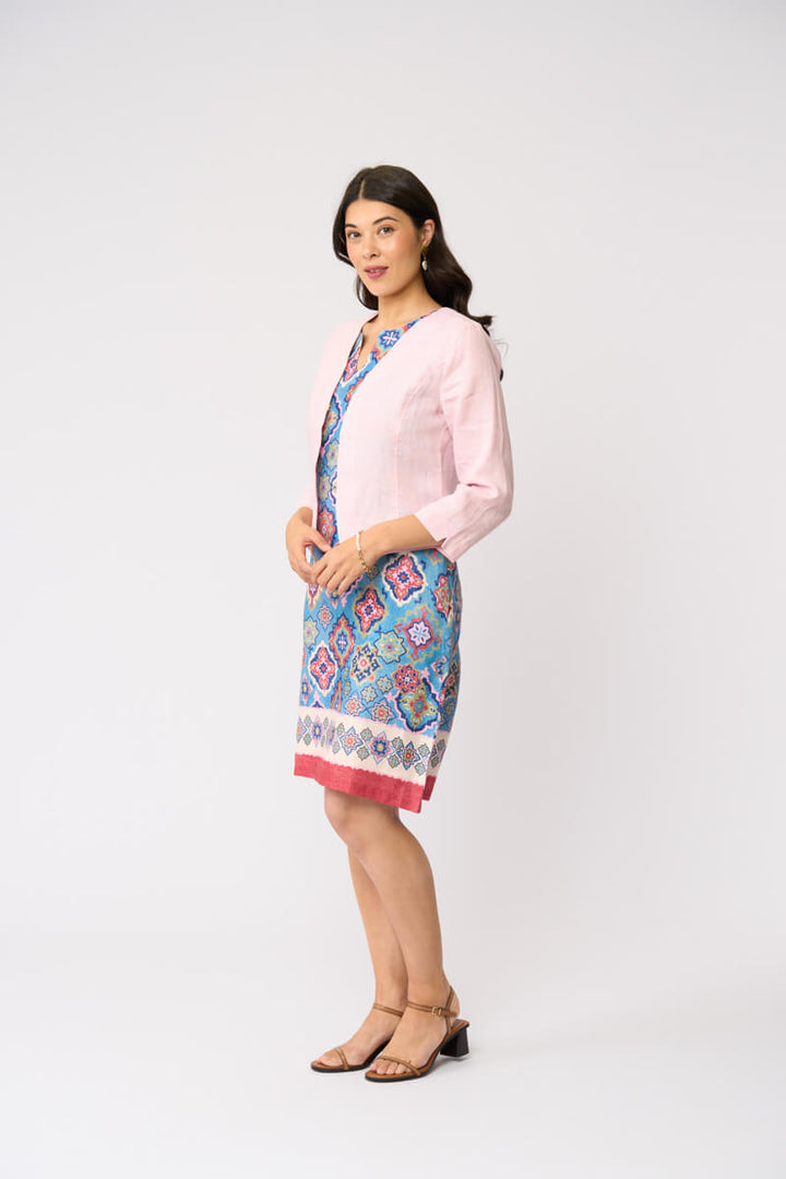 Foil model in a light pink cardigan over a blue and red patterned dress, standing against a plain white studio background.
