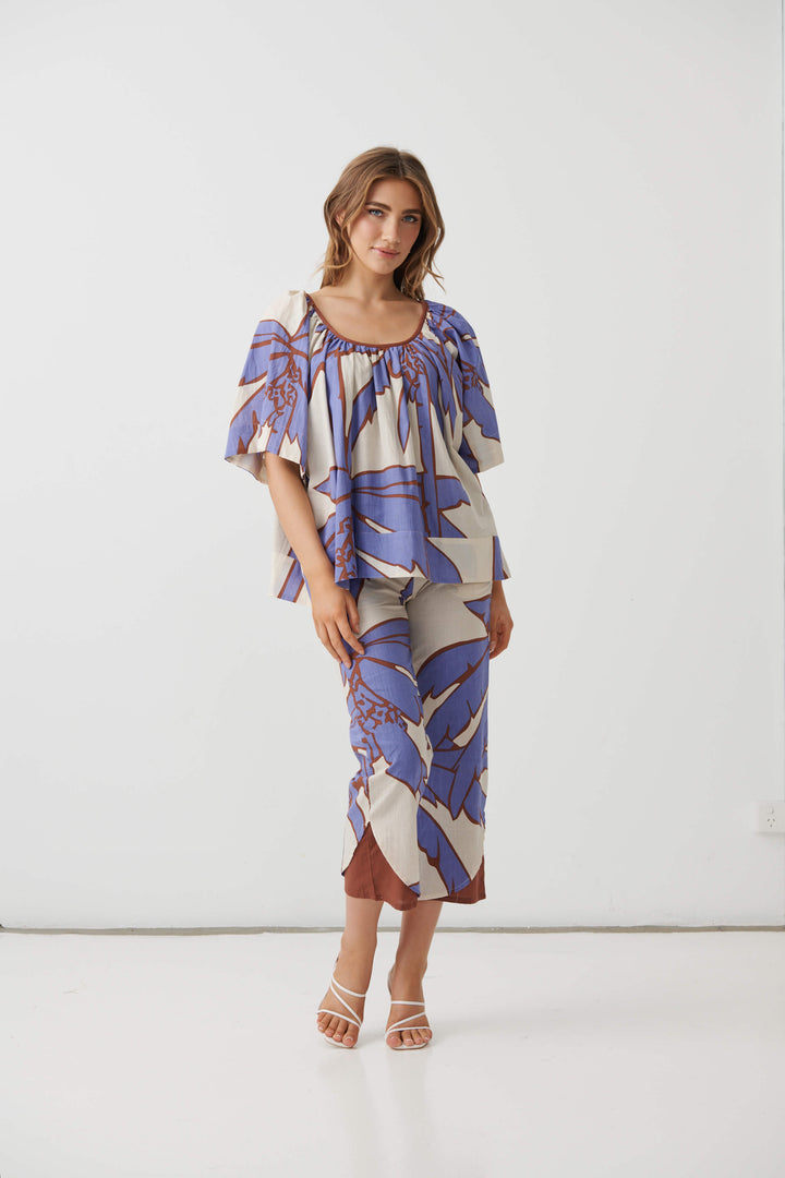 Holmes &amp; Fallon woman modeling a matching two-piece set featuring a short-sleeve top and cropped pants in a blue and brown botanical pattern on a cream background, paired with white heeled sandals. White studio background