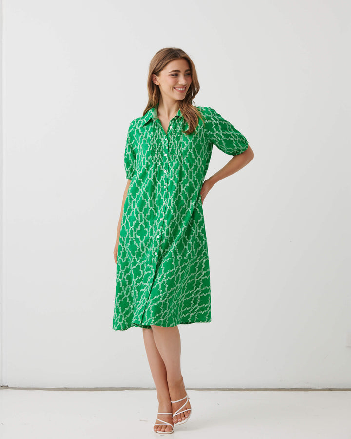 Homes &amp; Fallon woman modeling a green short-sleeve collared dress with a white geometric trellis pattern, standing against a plain white studio background.