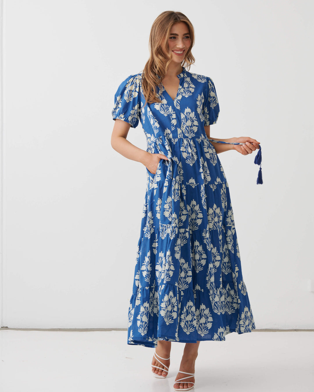 Holmes &amp; Fallon  woman modeling a blue and white floral print maxi dress with puff sleeves and a V-neckline, standing against a plain white studio background.