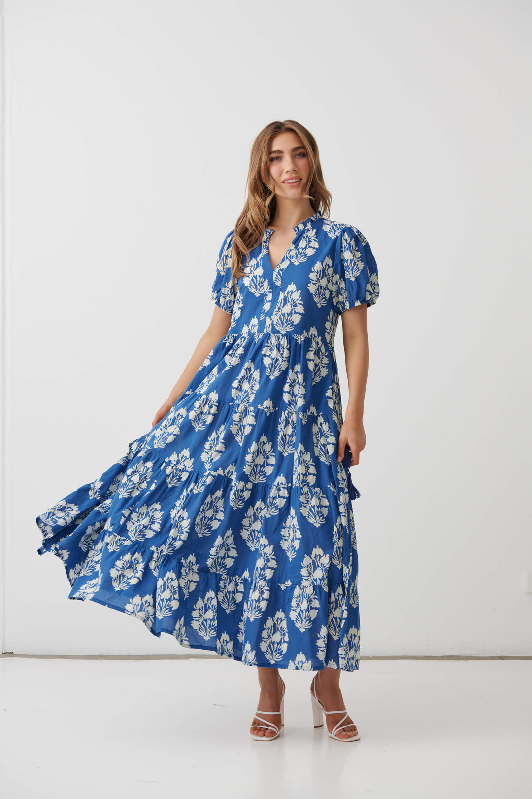 Holmes &amp; Fallon  woman modeling a blue and white floral print maxi dress with puff sleeves and a V-neckline, standing against a plain white studio background.