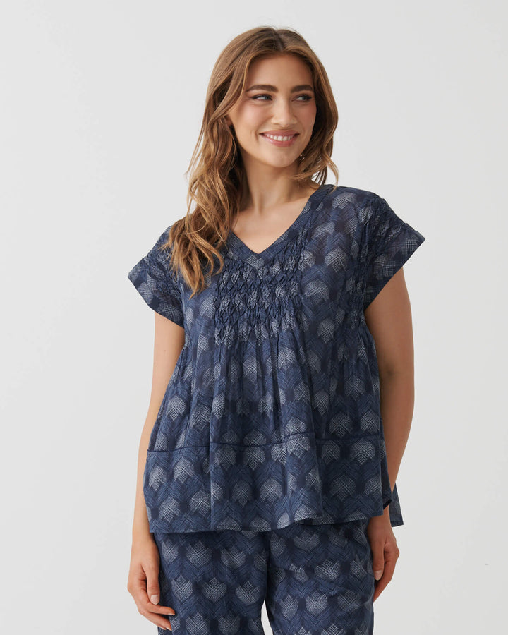 Holmes &amp; Fallon woman modeling a matching two-piece lounge set consisting of a smocked short-sleeve top and wide-leg cropped pants, both in navy blue with a light blue floral pattern, set against a plain white studio background.