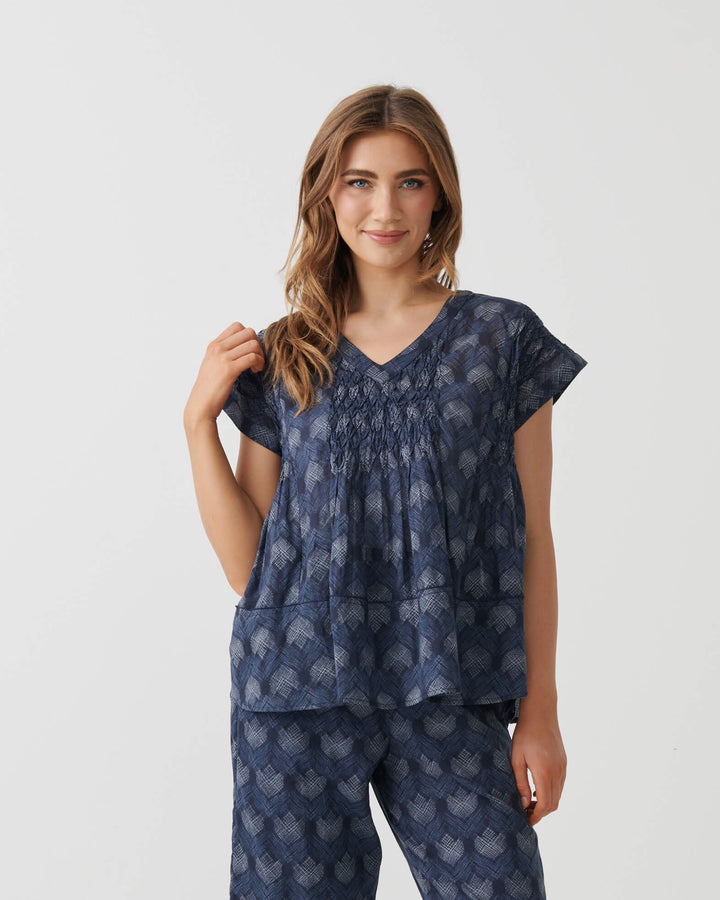 Holmes &amp; Fallon woman modeling a matching two-piece lounge set consisting of a smocked short-sleeve top and wide-leg cropped pants, both in navy blue with a light blue floral pattern, set against a plain white studio background.