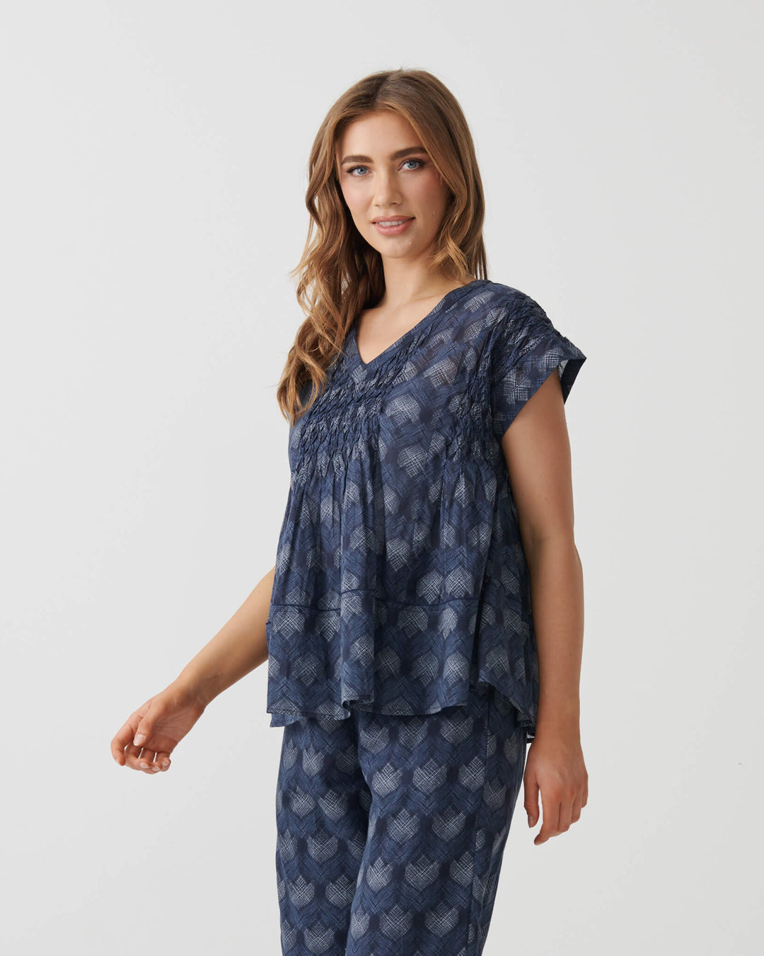 Holmes &amp; Fallon woman modeling a matching two-piece lounge set consisting of a smocked short-sleeve top and wide-leg cropped pants, both in navy blue with a light blue floral pattern, set against a plain white studio background.
