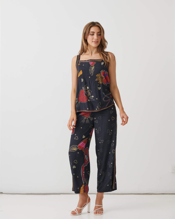Holmes and Fallon woman modeling a matching two-piece pajama set with a dark navy blue base and a colorful abstract print, consisting of a sleeveless top and wide-leg pants, against a plain white studio background.
