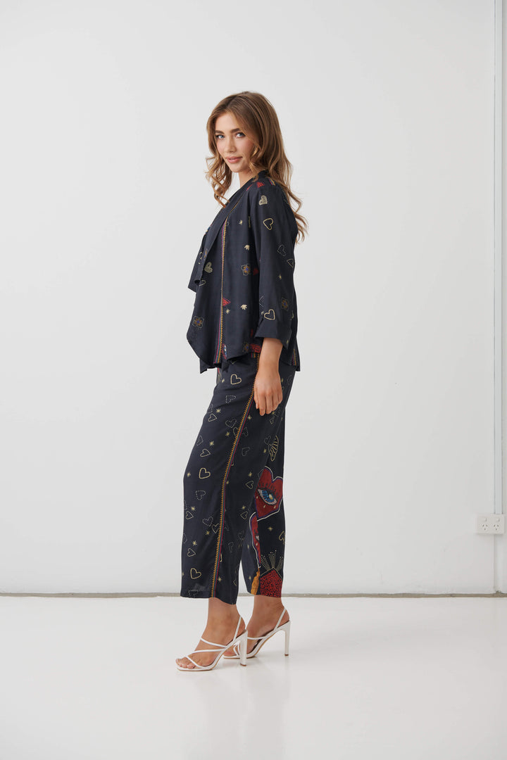 Holmes &amp; Fallon  woman modeling a dark navy two-piece lounge set with a colorful abstract print, consisting of a short-sleeve top and matching wide-leg pants, paired with a black tank top and beige strappy heels. On a white studio background