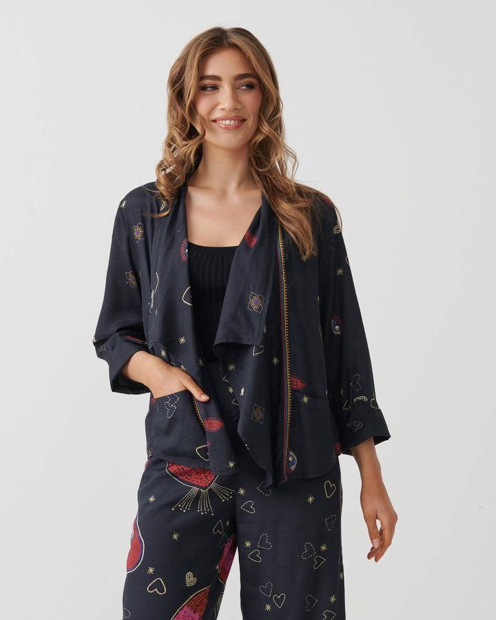 Holmes &amp; Fallon  woman modeling a dark navy two-piece lounge set with a colorful abstract print, consisting of a short-sleeve top and matching wide-leg pants, paired with a black tank top and beige strappy heels. On a white studio background