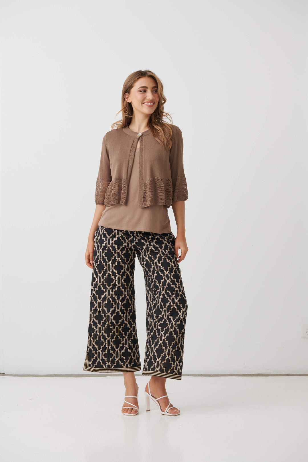 Holmes &amp; Fallon  modeling a brown textured three-quarter sleeve top paired with black wide-leg pants featuring a beige trellis pattern, standing against a plain white studio background.