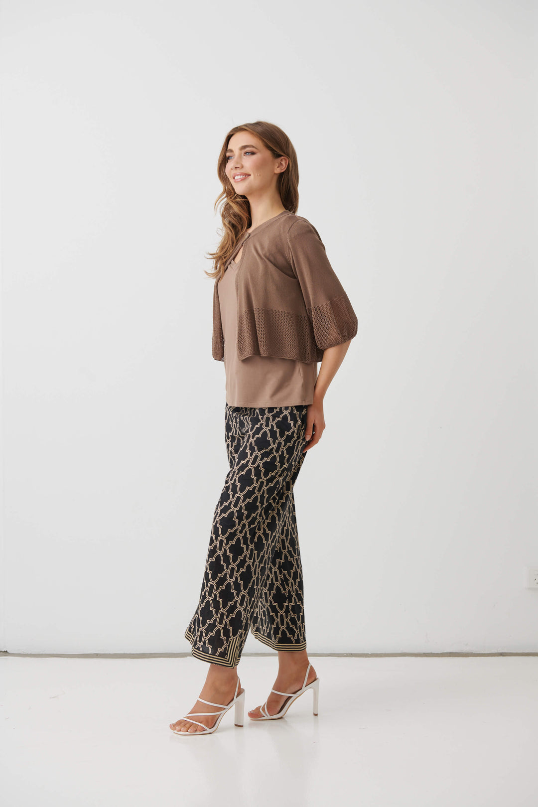 Holmes &amp; Fallon  modeling a brown textured three-quarter sleeve top paired with black wide-leg pants featuring a beige trellis pattern, standing against a plain white studio background.
