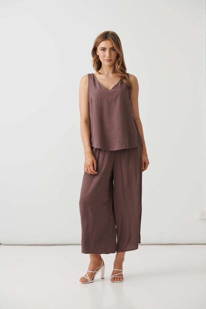 Holmes &amp; Fallon model in a mocha brown sleeveless V-neck swing top with smooth drape and layered-look hem. On a white studio background