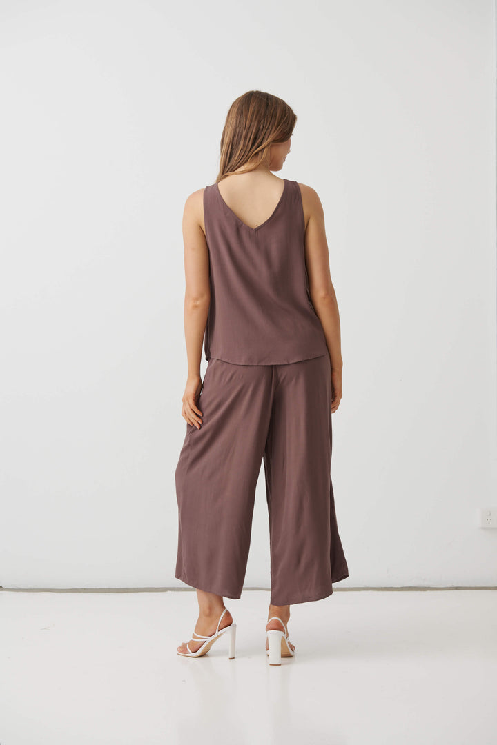 Holmes &amp; Fallon model in a mocha brown sleeveless V-neck swing top with smooth drape and layered-look hem. On a white studio background. Back view 