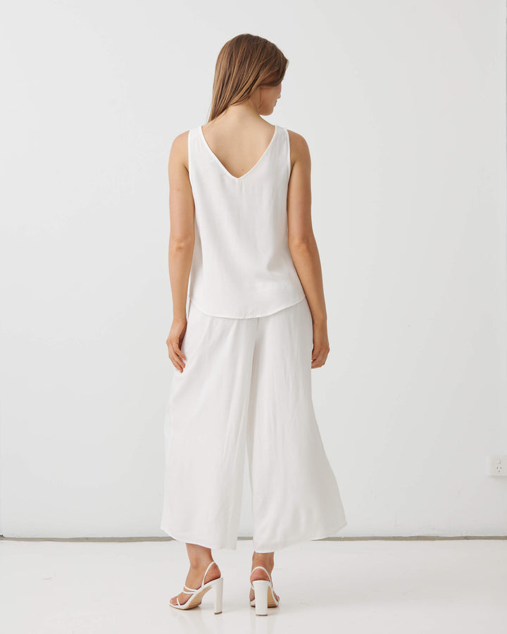 Holmes &amp; Fallon modeling a white sleeveless V-neck top and matching white wide-leg cropped pants, paired with white strappy high-heeled sandals, against a plain white studio background. Back view 