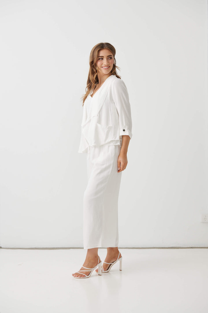 Holmes &amp; Fallon modeling a white two-piece outfit consisting of a draped long-sleeve blouse and matching wide-leg cropped pants, paired with strappy high-heeled sandals against a plain white studio background.
