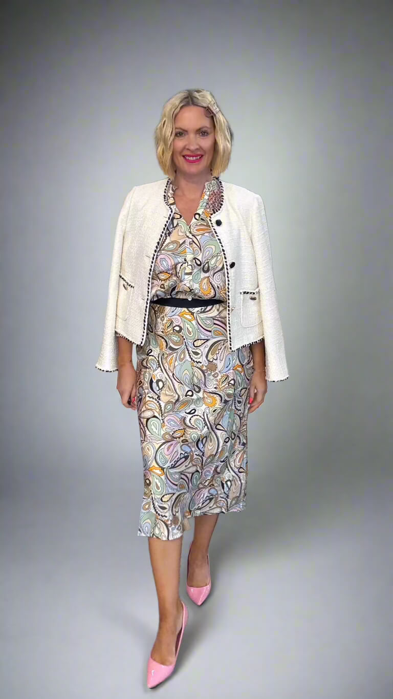 A woman modeling a coordinated outfit consisting of a white cropped jacket with black trim over a multicolor abstract print dress, paired with pink pointed-toe heels, against a neutral gray studio background. Mos Mosh Arzu Skirt at The Wardrobe