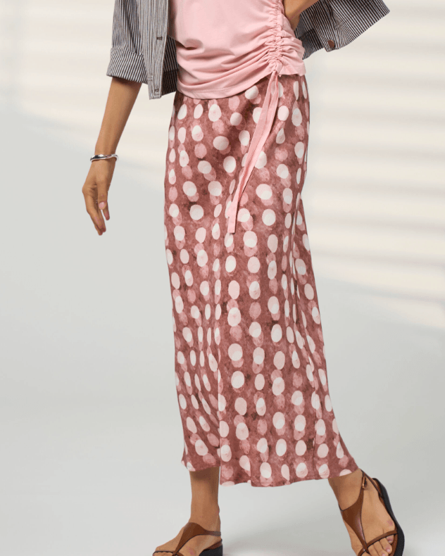 Madly Sweetly model in a pink midi skirt with allover white dot print and elastic gathered waist. On a studio background