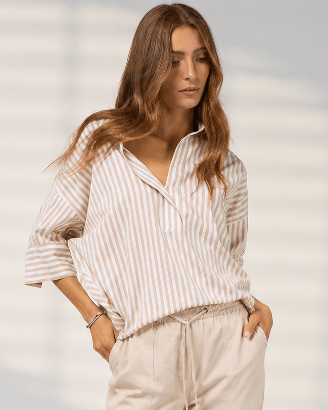 Madly Sweetly model  wearing light beige drawstring cropped pants with a striped shirt and brown sandals, standing against a light gray studio background with soft window-like shadows.