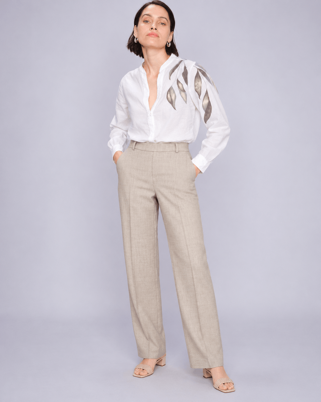 Mos Mosh  woman modeling a white long-sleeve blouse with metallic gold leaf embroidery on the shoulders, paired with beige wide-leg trousers and nude heeled sandals, against a light gray studio background.