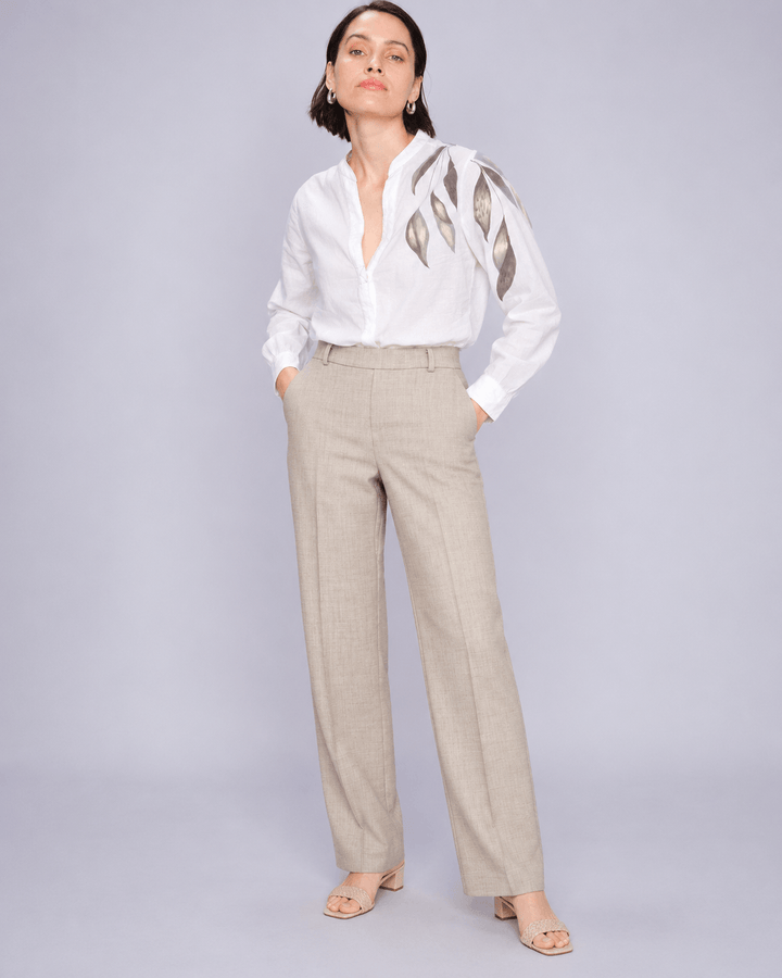 Mos Mosh  woman modeling a white long-sleeve blouse with metallic gold leaf embroidery on the shoulders, paired with beige wide-leg trousers and nude heeled sandals, against a light gray studio background.