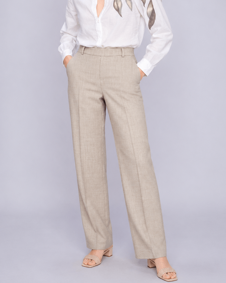 Mos Mosh  woman modeling a white long-sleeve blouse with metallic gold leaf embroidery on the shoulders, paired with beige wide-leg trousers and nude heeled sandals, against a light gray studio background.