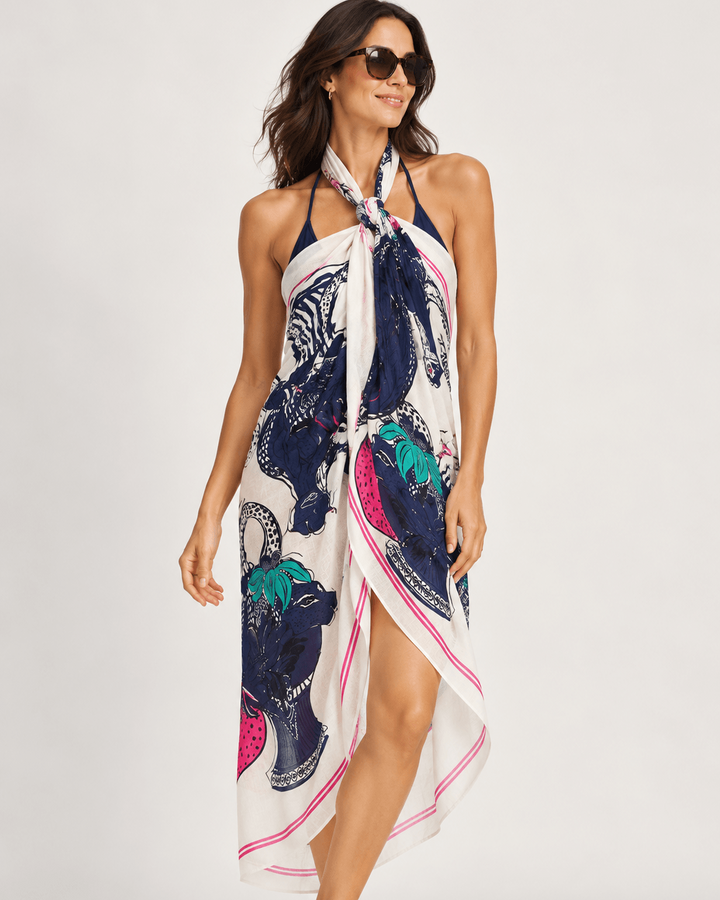 Pom Amsterdam woman modeling a halter wrap dress with a bold animal print. The dress features a cream base with navy blue, teal, and hot pink leopard and cheetah patterns, styled with dark sunglasses against a plain light gray studio background.