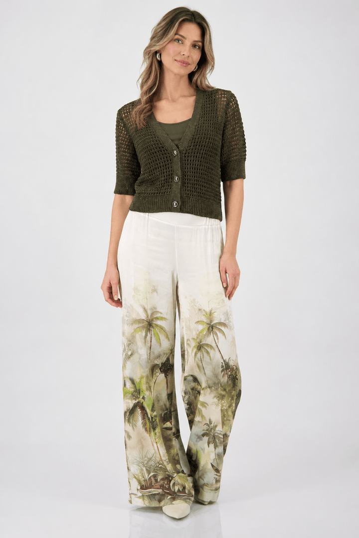 Monari woman modeling a short-sleeve olive green knit cardigan over a matching olive green top, paired with wide-leg white pants featuring a green and beige palm tree print, against a light gray studio background.