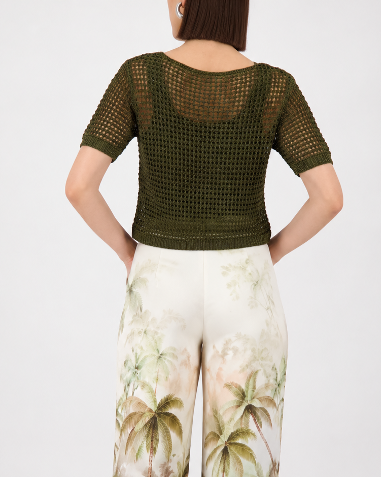 Monari  modeling a short-sleeve olive green knit top paired with white wide-leg pants featuring a green palm tree print, set against a plain light gray studio background.