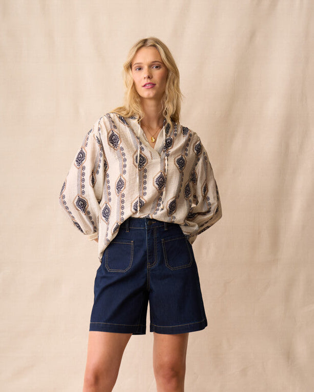 Neris model wearing a patterned blouse and navy shorts against a beige background