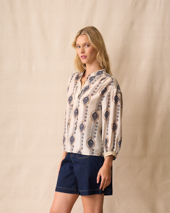Neris model wearing a patterned blouse and navy shorts against a beige background